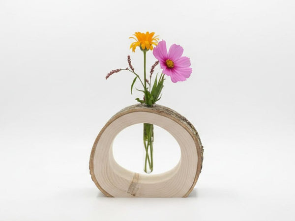 A rustic circular wooden slice vase holding two small flowers, one yellow and one pink, against a clean white studio background.